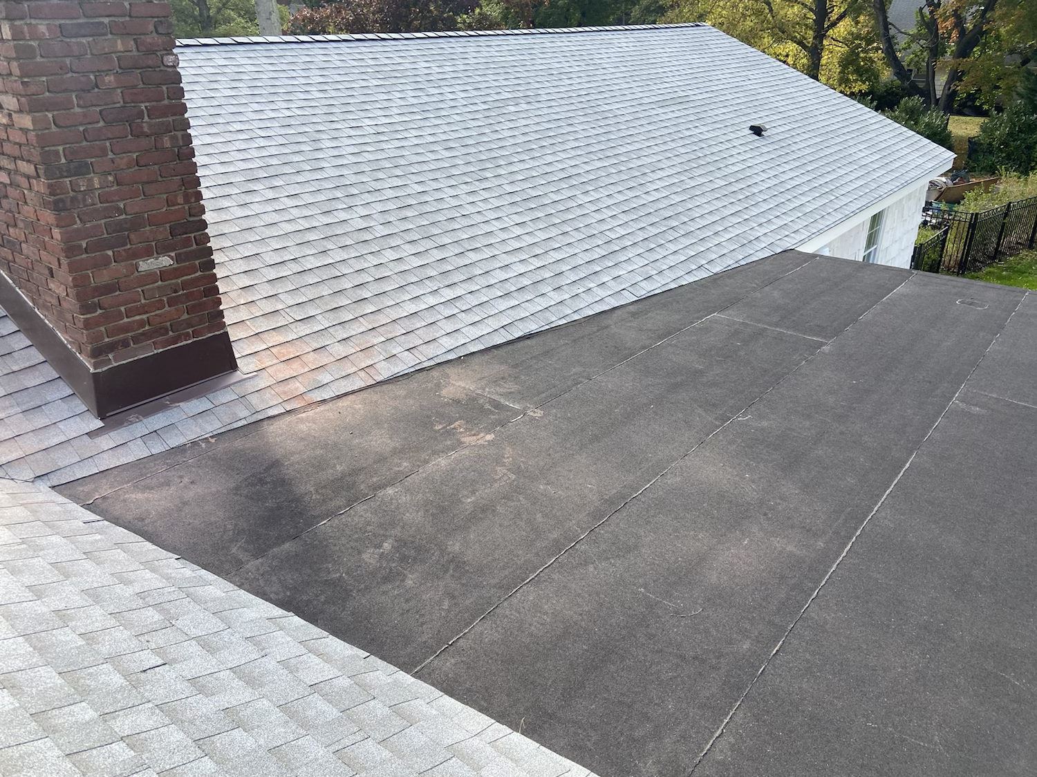 Flat roof section beside a shingled slope